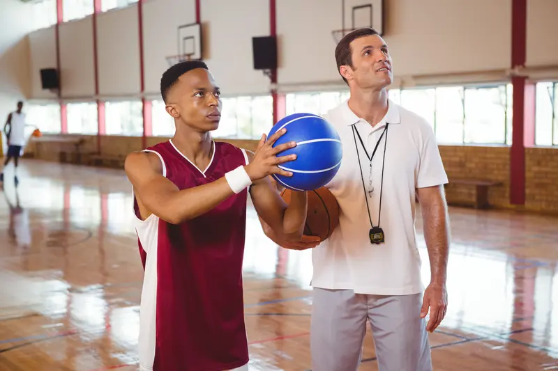Basketball coach providing one-on-one training instruction to a teenage boy on an indoor court