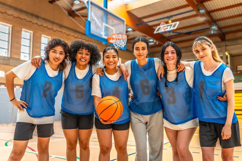 Female basketball team smiling and embracing each other on the court