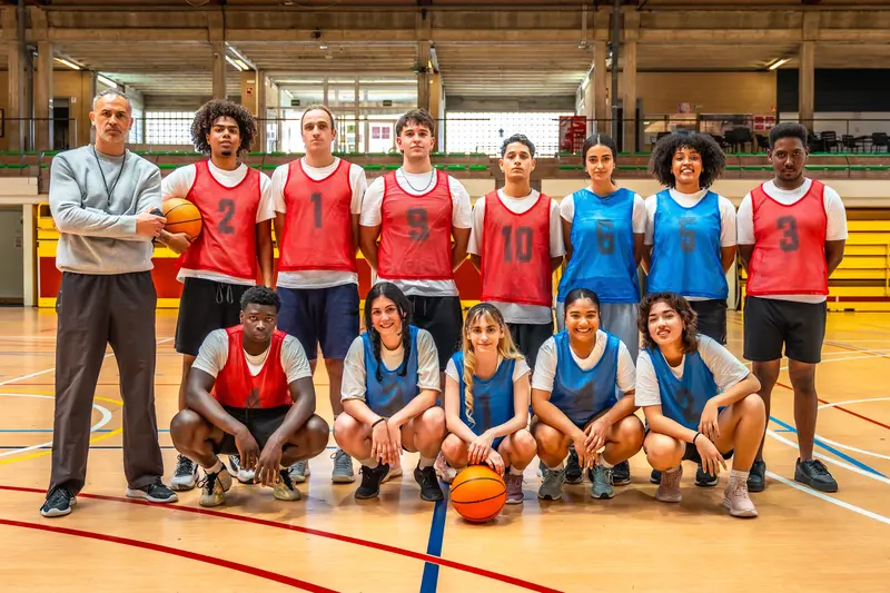 A high school basketball team posing together with their coach in a gymnasium